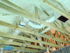 Spray foam insulation is installed in the attic in this picture, among roof beams and HVAC ducts.